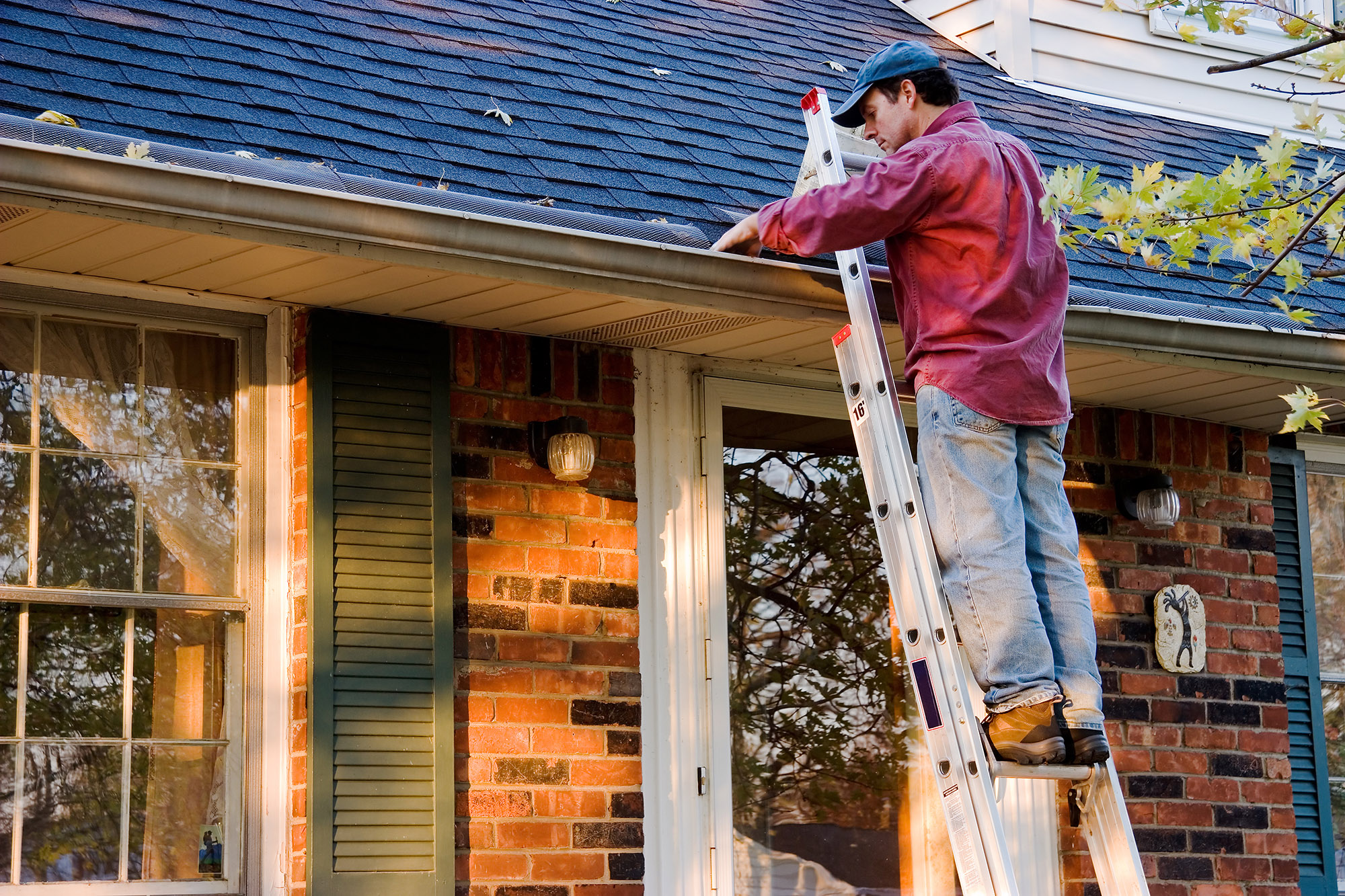 Man cleaning rain gutter on ladder