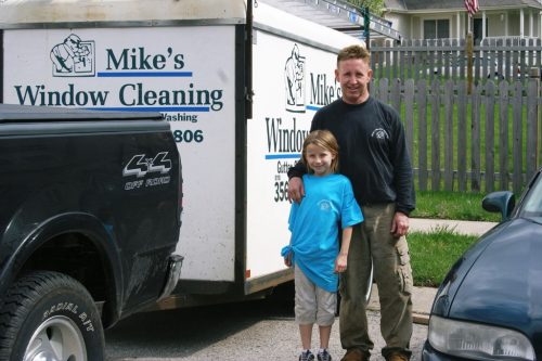 Technician from Mike's Window and Gutter Cleaning posing in front of work truck with child