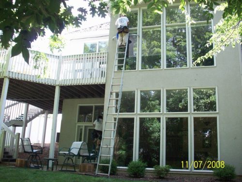Technician from Mike's Window and Gutter Cleaning cleaning exterior second story windows on Kansas City home